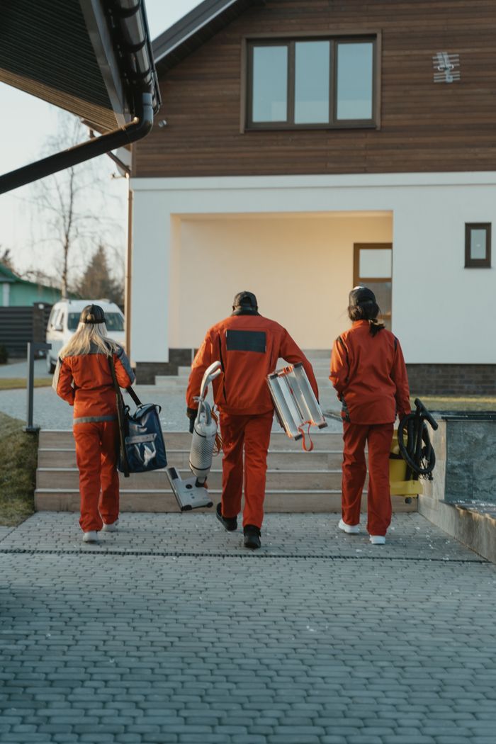 about-us-02 Cleaning crew in red uniforms with equipment approaching a modern house exterior.